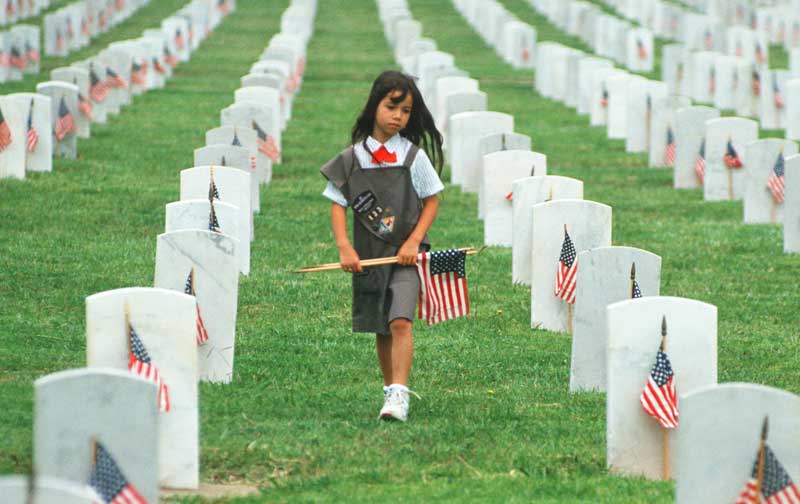 young girl walks through a military cemetery carrying an American flag