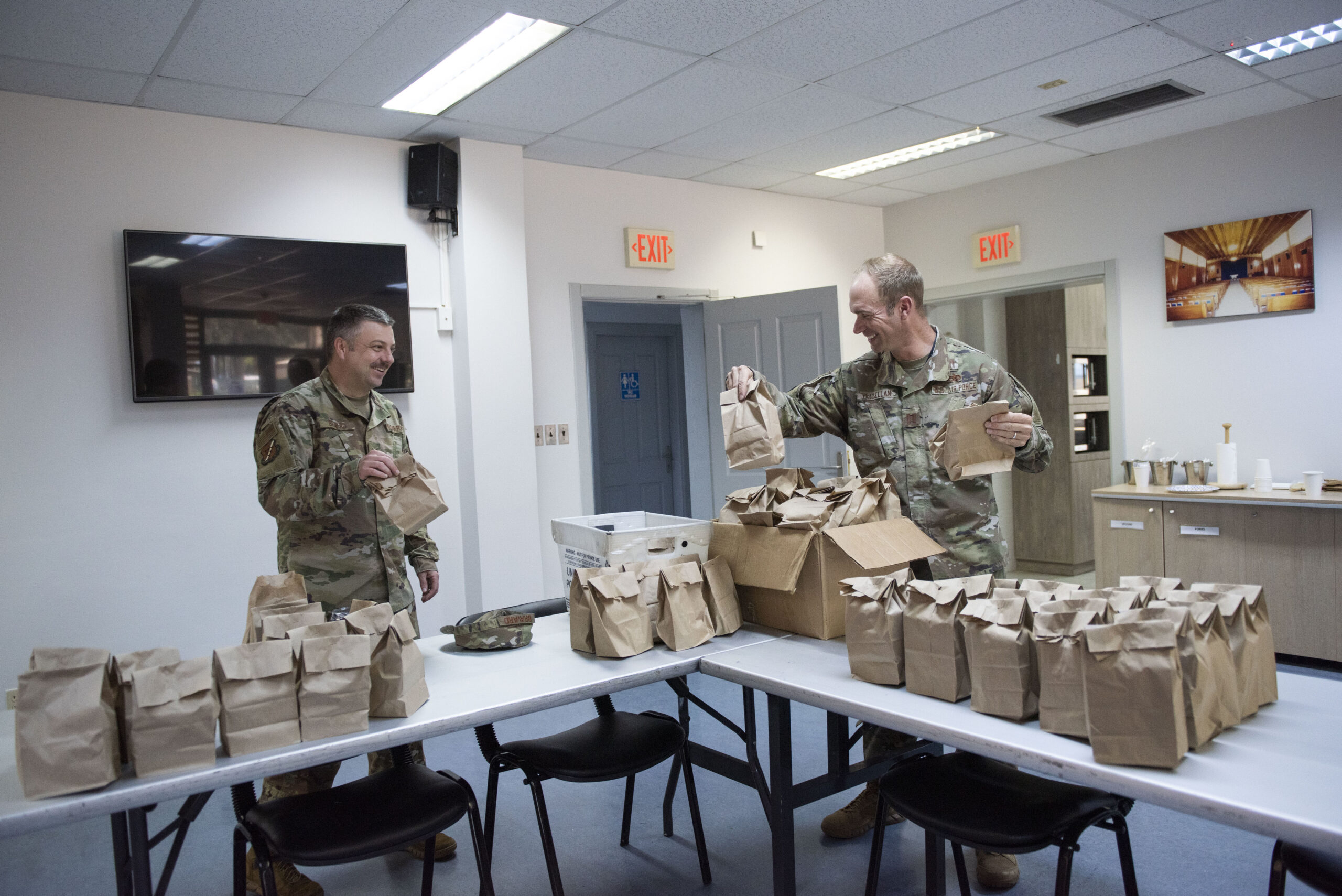 Service members, smiling, box meals in brown paper bags
