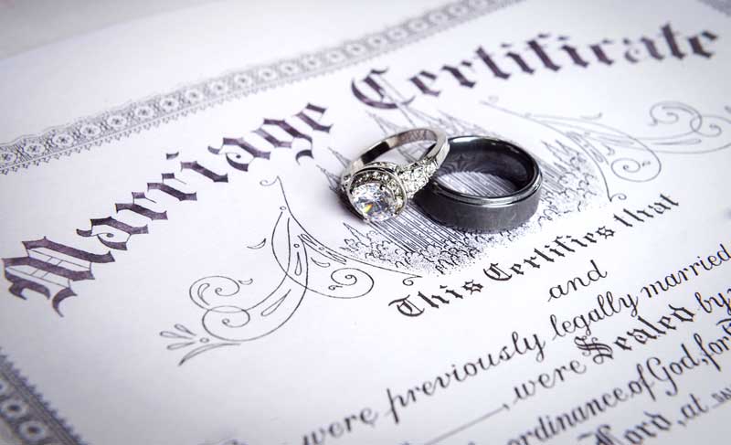 military couple's wedding rings on top of their marriage certificate