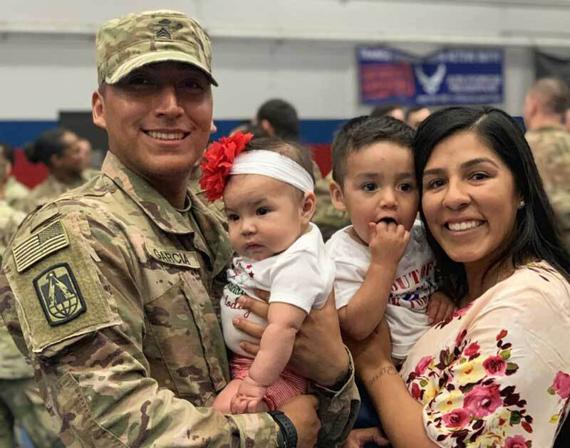 soldier smiles for a photo with his wife and children