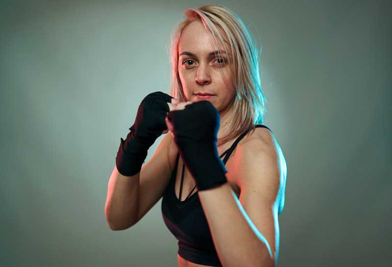 blonde woman with raised, taped fists confidently looks at camera