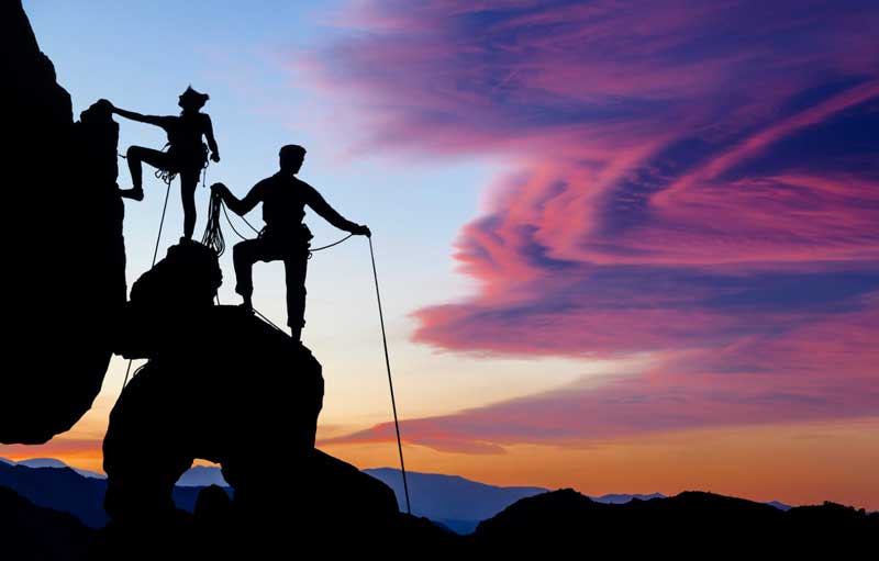 two people cast in shadow climbing mountain